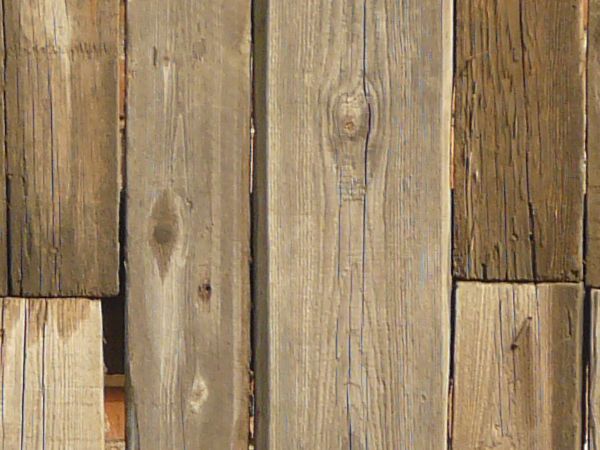 Uneven brown planks with crooked edges and dark spots set vertically with large gaps in between.